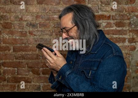 Latin American man (44) with long gray hair smiles while talking on his cell phone. Concept of technology Stock Photo