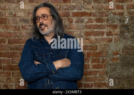 Latin American man (44) with long gray hair, blue jeans jacket and crossed arms. Copy space. Brick background. Lifestyle concept Stock Photo