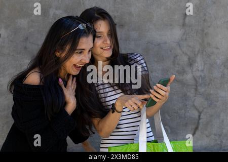 Latin American mother (50) and daughter (24) look at a post on the cell phone and the mother shows surprise. Mother's day concept and technology. Stock Photo