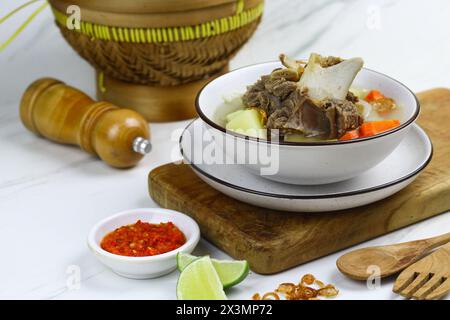 Sop daging sapi or Indonesian beef soup, served on ceramic white bowl with sambal and slices of lime. Selective focus with white marble background. Stock Photo