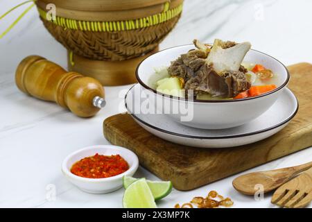 Sop daging sapi or Indonesian beef soup, served on ceramic white bowl with sambal and slices of lime. Selective focus with white marble background. Stock Photo