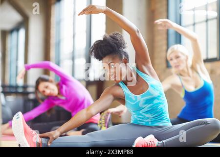 Black woman, instructor and yoga class at gym, stretch and yogi trainer for exercise on mat. Female person, floor and confident for pilates or Stock Photo