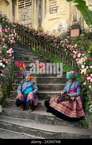 Flower Hmong women sitting on the stairs of the Hmong Kings Palace (Vau Meo) in Bac Ha, Lao Cai Province, Vietnam Stock Photo