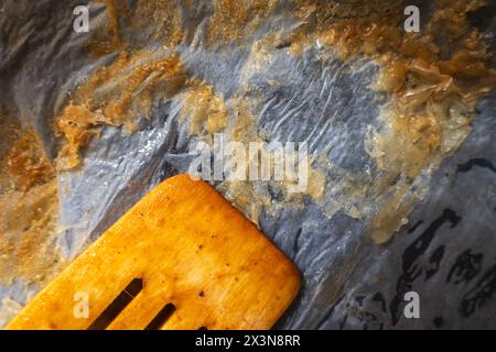 Used dirty wooden mixing spoon inside empty tray lined with baking paper. Stock Photo