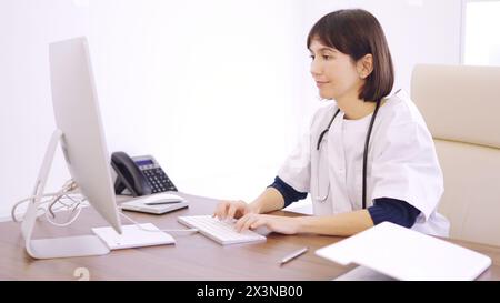 Doctor using computer sitting on a desk in a clinic Stock Photo