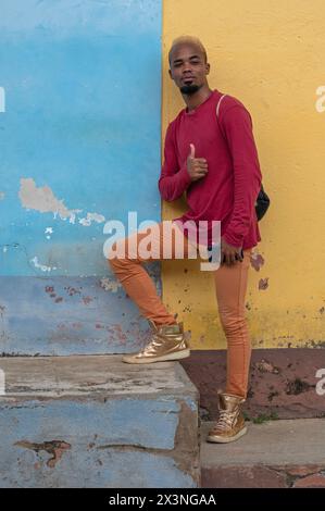 Young man holding a mobile phone happily posing to have his picture taken in the backstreets of the Old Town, Trinidad, Cuba. Stock Photo