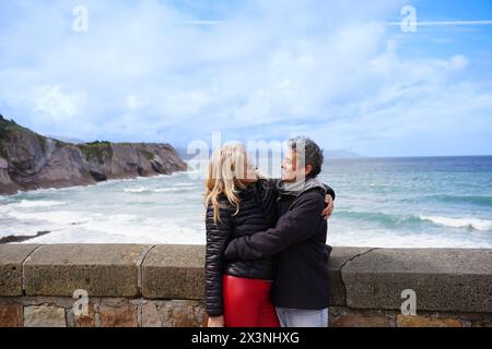 A gay women couple is standing on a beach, smiling at each other. A happy and relaxed family Stock Photo