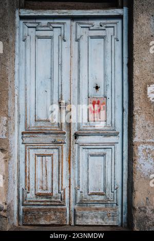 Old wooden door with peeling paint, and a red smiley painted on it of dilapidated house in Kala, Tbilisi Old town, Georgia Stock Photo