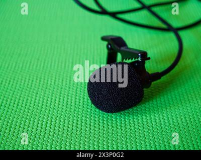 Audio Recording Gear. Wired lapel mic with clip against a green textured surface. Stock Photo