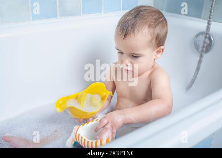 Toddler giggles while playing with bathwater, creating splashes and smiles in the tub. Stock Photo