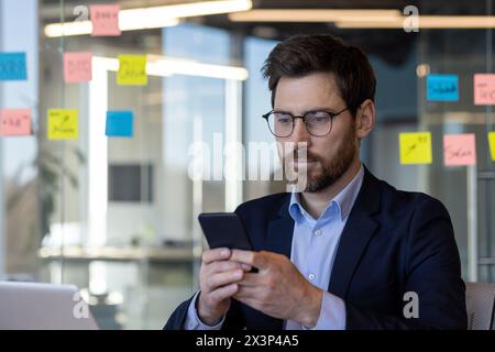 A man in a suit is looking at his cell phone. Concept of modernity and technology, as the man is using his phone in a professional setting. The man's facial expression Stock Photo