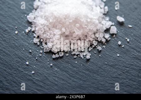White salt cristals for food on the black background. Pile of sea salt good igredient on the kitchen. Stock Photo
