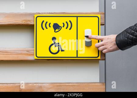 a person's hand presses the button to call staff helping people with limited mobility. woman presses doorbell button. yellow shield with call button. Stock Photo