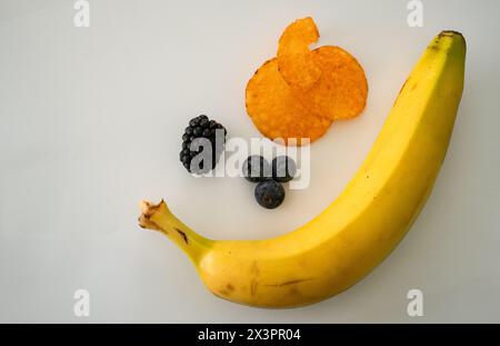 Assortment of a banana, a blackberry, three blueberries, and some potato chips. You have choices. Stock Photo