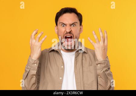 Frustrated Man Expressing Anger With Raised Hands Against Yellow Background Stock Photo