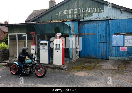 Motorcyclist on a custom built motorbike at an old disused garage in Much Wenlock, Shropshire Stock Photo