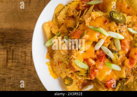 Close up top view of nachos with meat and cheese on a white plate on a wooden table Stock Photo