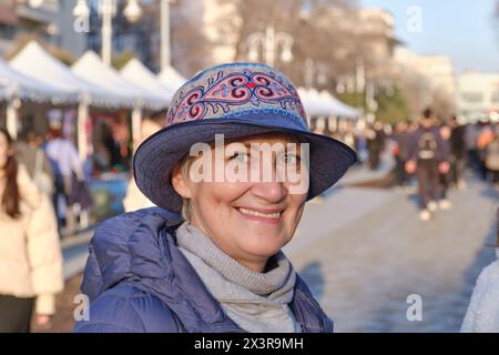 Portrait of senior Caucasian woman, wearing felt hat with Kazakh embroidered pattern, at crafts fair Stock Photo