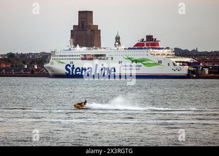 A jetski rider races up the River Mersey in Liverpoool with the Belfast ferry docked on the Wirral shore Stock Photo