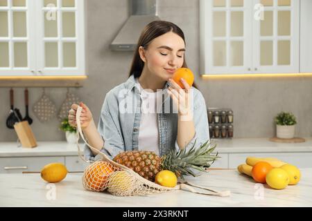Woman with string bag of fresh fruits at light marble table in kitchen Stock Photo