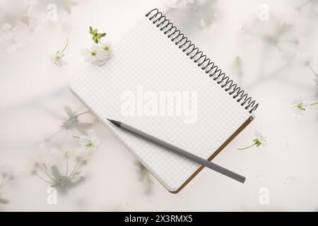 Guest list. Notebook, pencil and beautiful cherry tree blossoms on spring floral background, flat lay Stock Photo