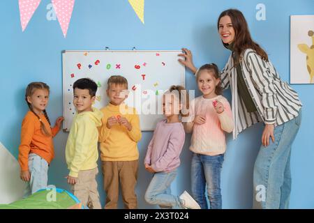Little children and nursery teacher with magnetic board in kindergarten Stock Photo