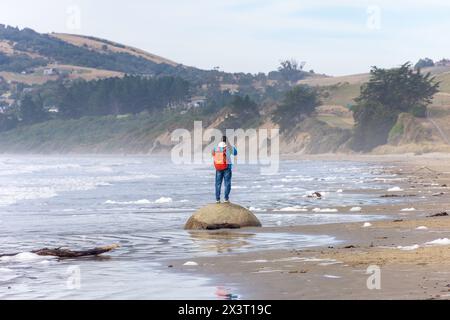 Young woman standing on Moeraki Boulder on Moeraki Boulders (Kaihinaki) Beach, Moeraki, Otago, South Island, New Zealand Stock Photo