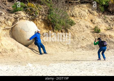 Tourists with Moeraki Boulder on Moeraki Boulders (Kaihinaki) Beach, Moeraki, Otago, South Island, New Zealand Stock Photo