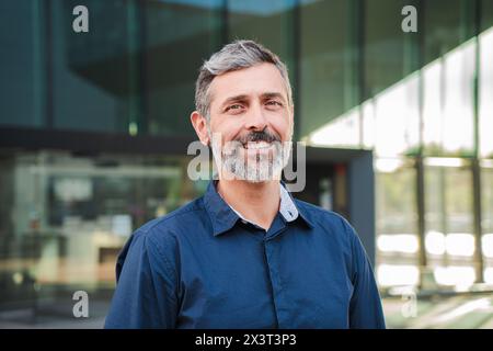 Bearded mature man smiling and looking at camera. Middle aged male entrepreneur staring front with friendly and confident expression. Individual portrait of a mid adult guy wearing blue shirt. High quality photo Stock Photo