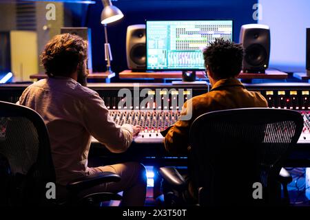 Singer and producer working together in professional music studio, collaborating on a hit song in control room. Audio engineer editing records with mixing and mastering techniques. Stock Photo