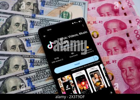 TikTok app seen on the screen of smartphone, which is placed on US dollars an Chinese Yuan banknotes. Stafford, United Kingdom, April 28, 2024 Stock Photo