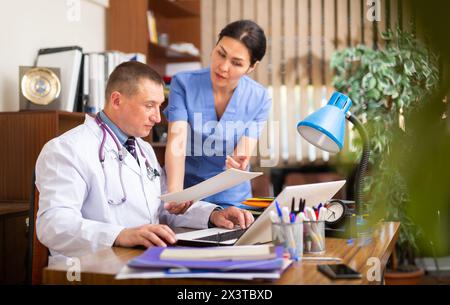 Two focused physicians working with case histories on laptop Stock Photo