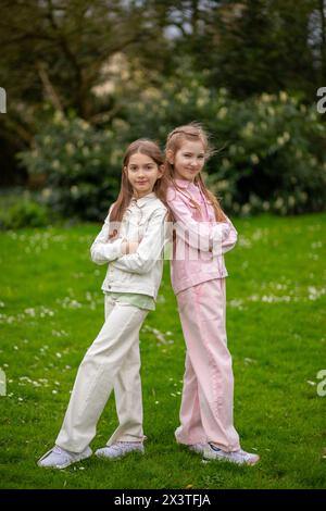 Two friendly girls in light-toned clothing with smiles enjoying a spring day in the park, standing on green grass Stock Photo
