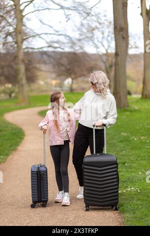 Mother and daughter facing each other, holding suitcases on a park path Stock Photo