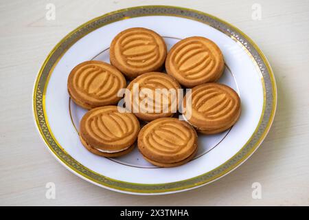 Delicious wheat biscuits filled with milk cream served on a white plate on wooden background. Stock Photo