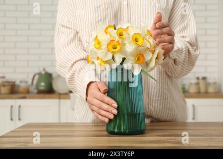 Young woman touching vase with yellow flowers on table in stylish kitchen Stock Photo