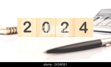 2024 The numbers are written on wooden cubes in a composition with a calculator, a pen on a white background Stock Photo