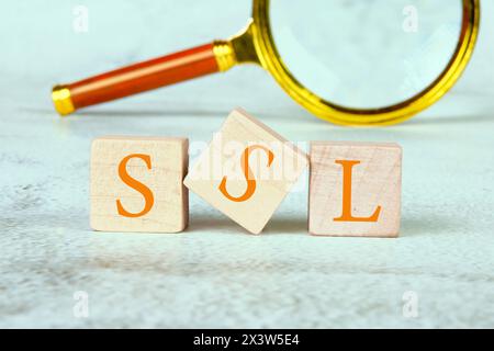 SSL (Secure Sockets Layer) text written on wooden cubes with a magnifying glass in the background Stock Photo