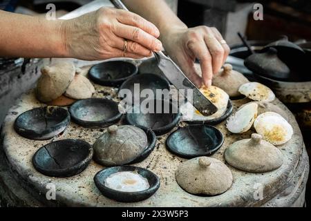 Vietnamese mini fried eggs, with rice flour, cooking on the street. Asian woman preparing Traditional Vietnamese breakfast. Banh can is a popular dish Stock Photo