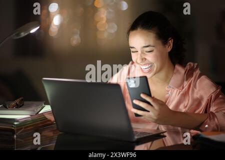 Happy tele worker in the night laughing hilariously checking phone at home Stock Photo