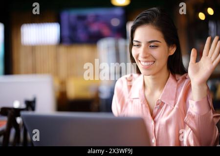 Happy self employed having video call with a laptop in a bar interior Stock Photo