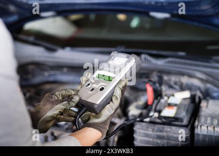 Female auto mechanic using diagnostic tool, scanner, running diagnostic on car. Beautiful woman working in a garage, wearing blue coveralls. Stock Photo