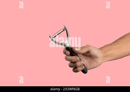 Black male hand holding a potato peeler isolated on pink background Stock Photo