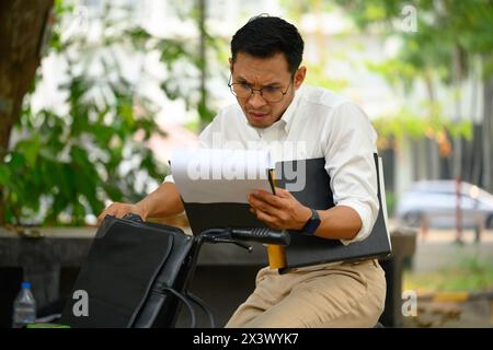 Serious busy businessman sitting on his bicycle and checking business documents Stock Photo