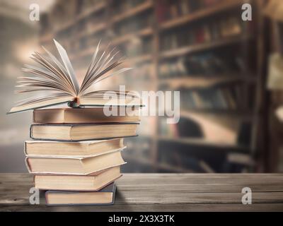 A stack of old books on a wooden surface against a background of bookshelves Stock Photo