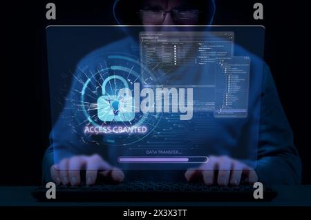 Man in hood on dark background uses keyboard and virtual screen to break cybersecurity system Stock Photo