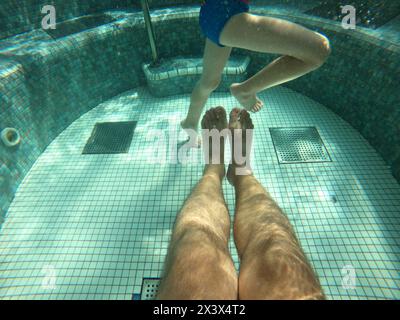 Hot tub pool, underwater shot of father and son legs in water, selective focus Stock Photo