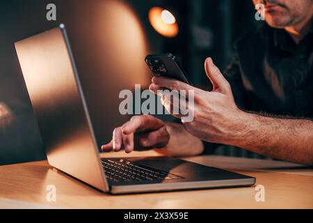 Multitasking with smartphones and laptop, businessman working in office late at night, selective focus Stock Photo