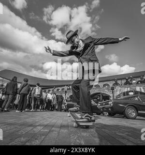 A black and white image of a well-dressed man in a pinstpriped suit having fun on a skateboard in London. Stock Photo