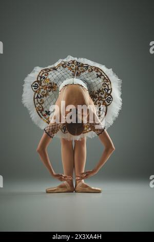 A young, beautiful ballerina in a white tutu is gracefully bending over. Stock Photo